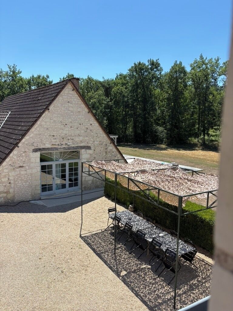 A stone building with a sloped roof, a covered outdoor seating area with tables and chairs, and a gravel ground.