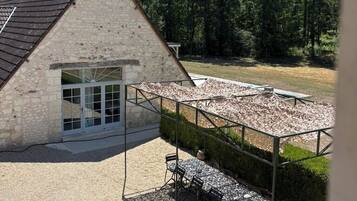 A stone building with a sloped roof, a covered outdoor seating area with tables and chairs, and a gravel ground.
