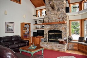 A cozy living room with a stone fireplace, leather sofa, and a bookshelf.
