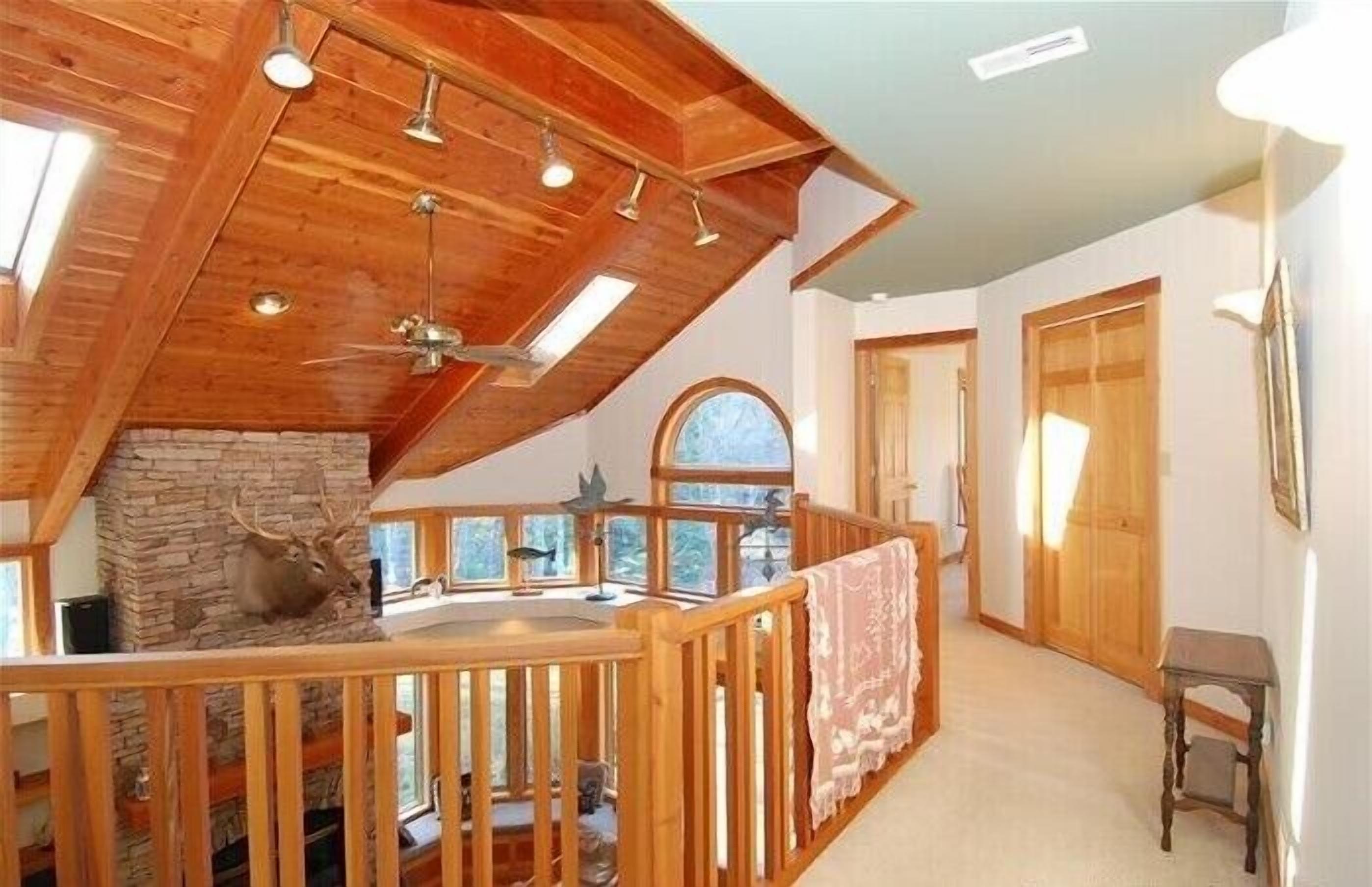 A cabin with a wooden interior, a stone fireplace, and a balcony with a railing.