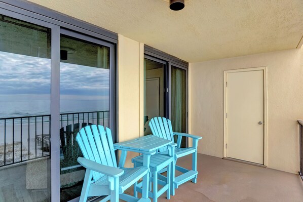 A balcony with a table and chairs, a door, and a view of the ocean.