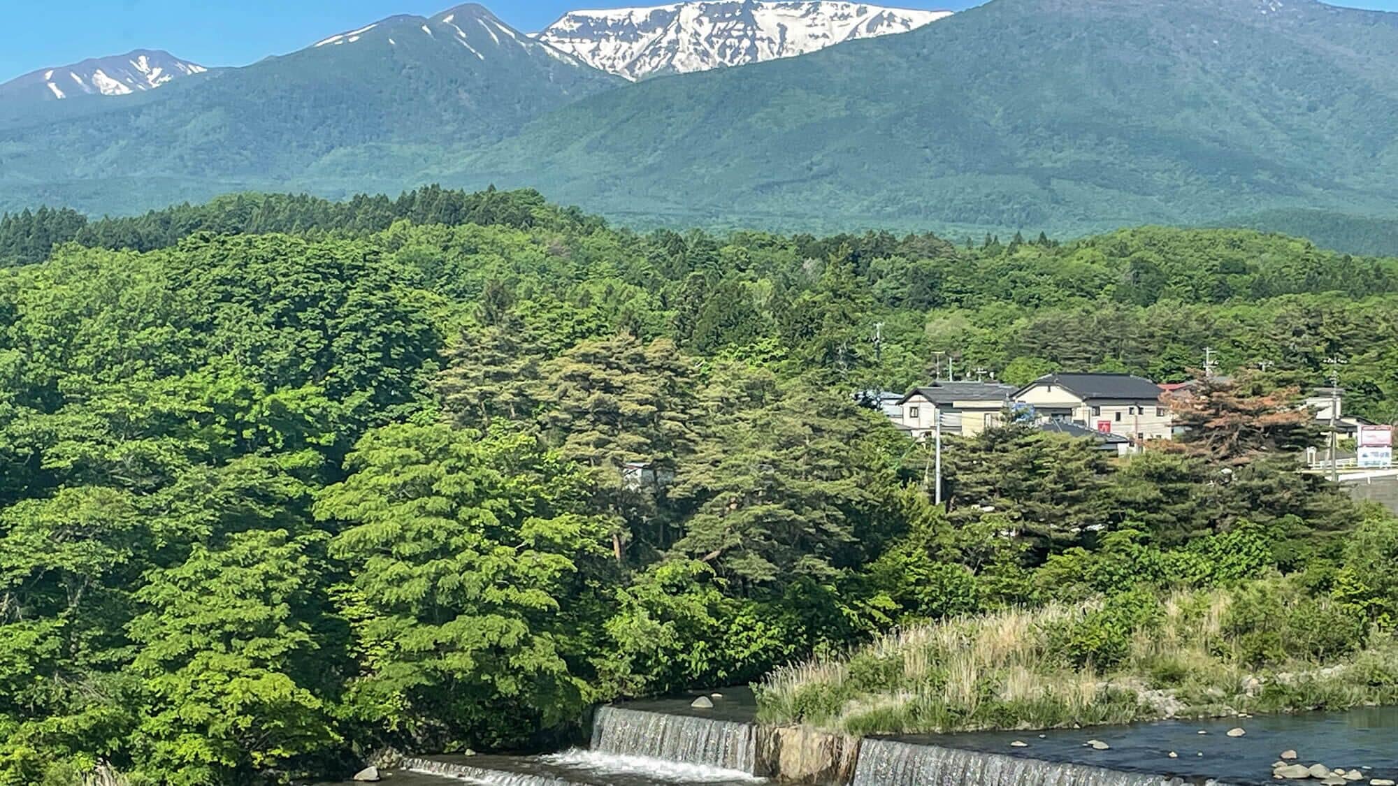 A mountainous landscape with dense forest, a small settlement, and a waterfall.