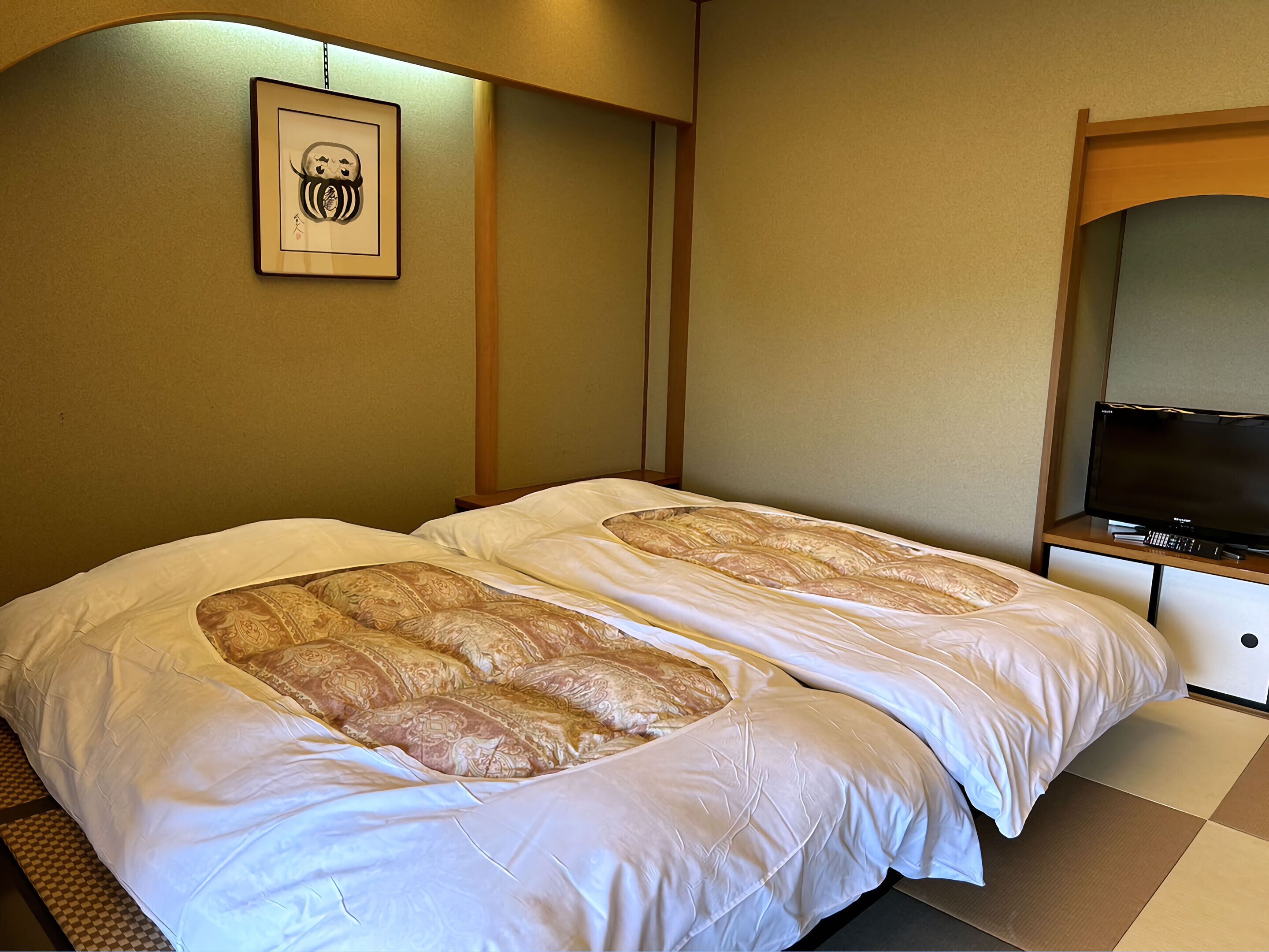 A hotel room with two beds, a television on a stand, and a framed picture on the wall.