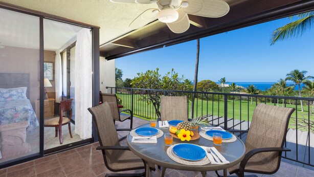 A balcony with a table set for two, chairs, a ceiling fan, and a view of the ocean. - 🏖️Keauhou Golf & Ocean View Condo w/ AC | Bridge-Level Entry (Kailua Kona)