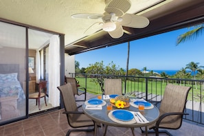 A balcony with a table set for two, chairs, a ceiling fan, and a view of the ocean.