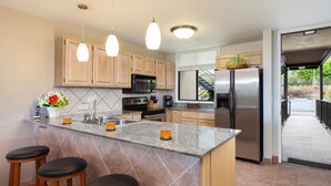 A modern kitchen with granite countertops, stainless steel appliances, wooden cabinets, and a bar area with stools. - 🏖️Keauhou Golf & Ocean View Condo w/ AC | Bridge-Level Entry (Kailua Kona)