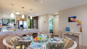 A modern kitchen with a dining area, featuring a glass-top table, wicker chairs, and a view of the backyard. - 🏖️Keauhou Golf & Ocean View Condo w/ AC | Bridge-Level Entry (Kailua Kona)