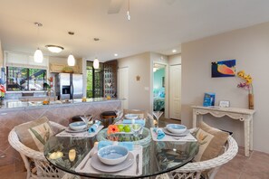 A modern kitchen with a dining area, featuring a glass-top table, wicker chairs, and a view of the backyard.