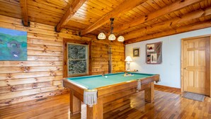 Ein Billardtisch aus Holz in einem Raum mit Holzwänden und -decke, einer Tür und einem Fenster mit Jalousien.