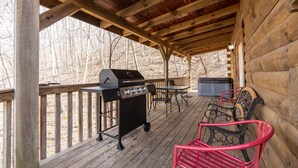 Eine überdachte Holzterrasse mit Grill, Sitzgelegenheiten und Blick auf den umliegenden Wald.