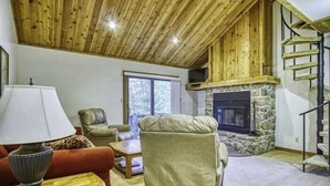 Ein gemütliches Wohnzimmer mit Kamin aus Stein, Holzboden und einer Treppe.