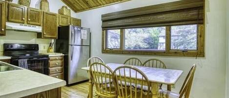 Una cocina con armarios de madera, una estufa, un refrigerador y una mesa de comedor con sillas.