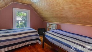 Ein Schlafzimmer mit zwei Betten, einem Fenster, einem Bücherregal und einem Deckenventilator.