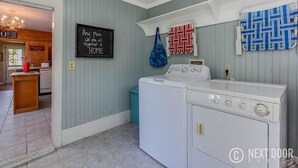 A laundry room with a washing machine and dryer, a chalkboard with a message, and a patterned towel on the wall.