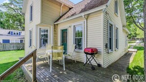 Ein zweistöckiges Haus mit überdachter Veranda, Grill und kleinem Tisch.
