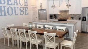 A modern kitchen with white cabinetry, a wooden dining table, and pendant lighting. - Amazing Grace: 7  BR, 5  BA House in Port Bolivar, Sleeps 25 (Port Bolivar)