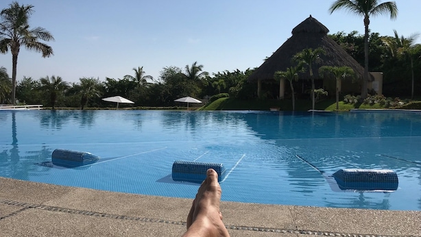 Una piscina con agua azul cristalina, sillas de descanso y palmeras.
