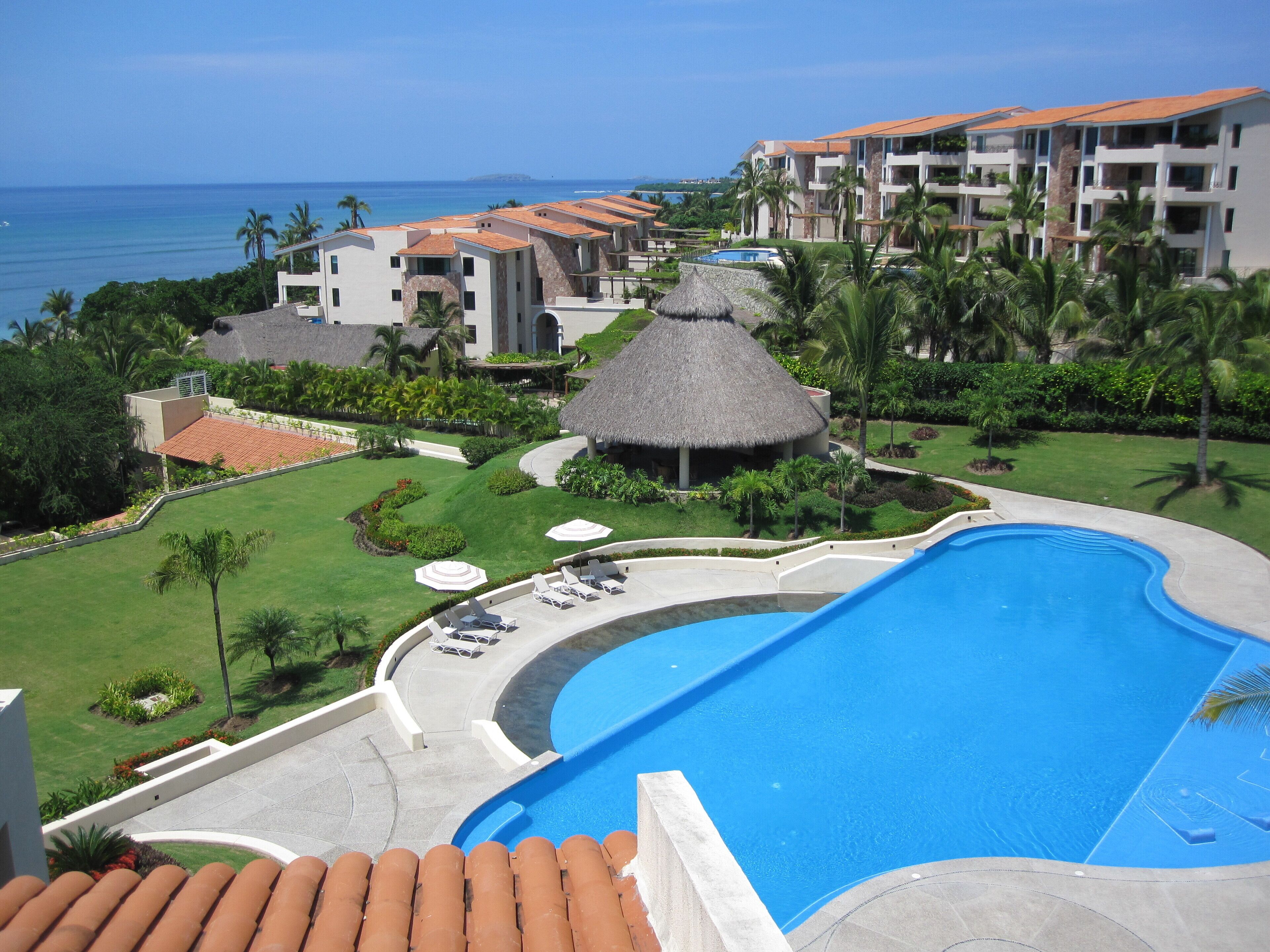 A resort with a swimming pool, palm trees, and a view of the ocean.