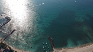 Vista aérea de una zona costera con aguas turquesas cristalinas, una playa arenosa y varios barcos anclados cerca de la orilla.