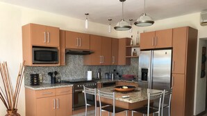 Una cocina moderna con armarios marrones, electrodomésticos de acero inoxidable y una isla central con taburetes de bar.