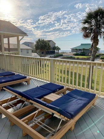 A deck with wooden lounge chairs and a white railing.