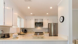 A modern kitchen with white cabinets, stainless steel appliances, and two woven stools.