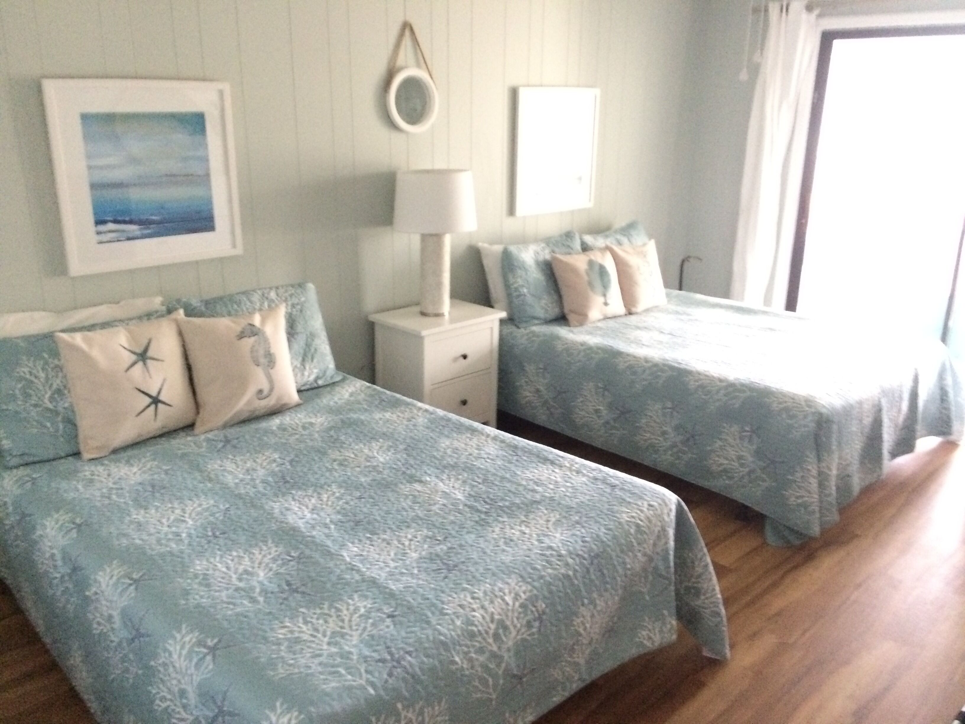 A bedroom with two beds, a nightstand, a lamp, and a framed picture on the wall.