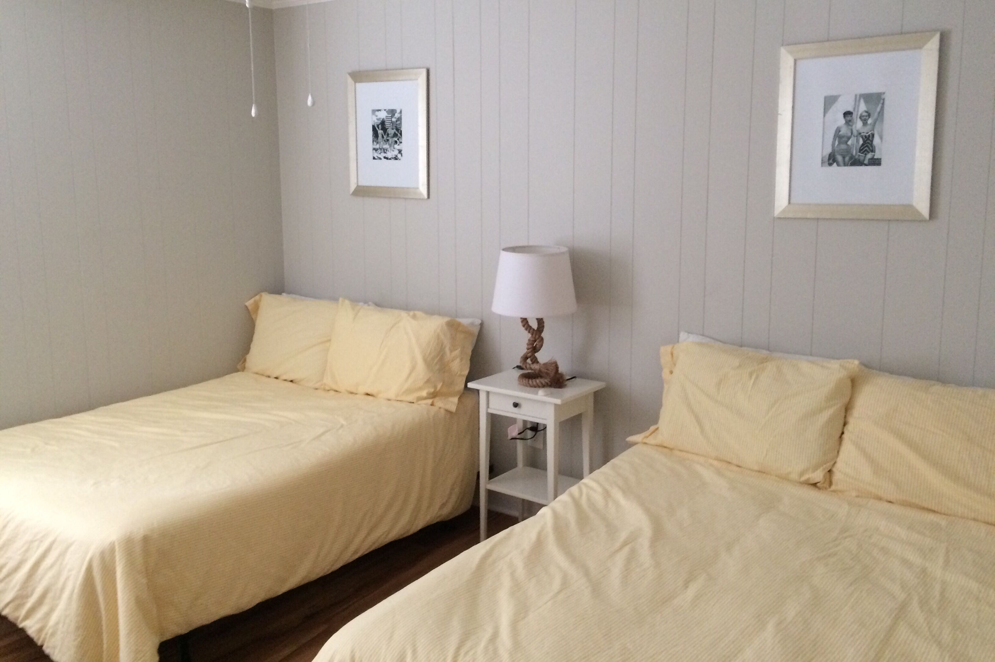 A room with two single beds, each with a white bedspread and matching pillows. There is a small bedside table with a lamp between the beds.