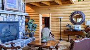 A log cabin interior with a stone fireplace, wooden furniture, and a balcony. - True Ski-in Ski-Out. (Brian Head)
