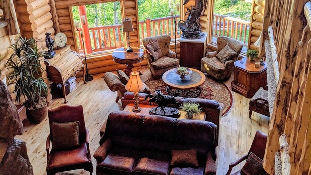 A cozy log cabin interior with a fireplace, leather sofas, and large windows offering a view of the forest. - True Ski-in Ski-Out. (Brian Head)