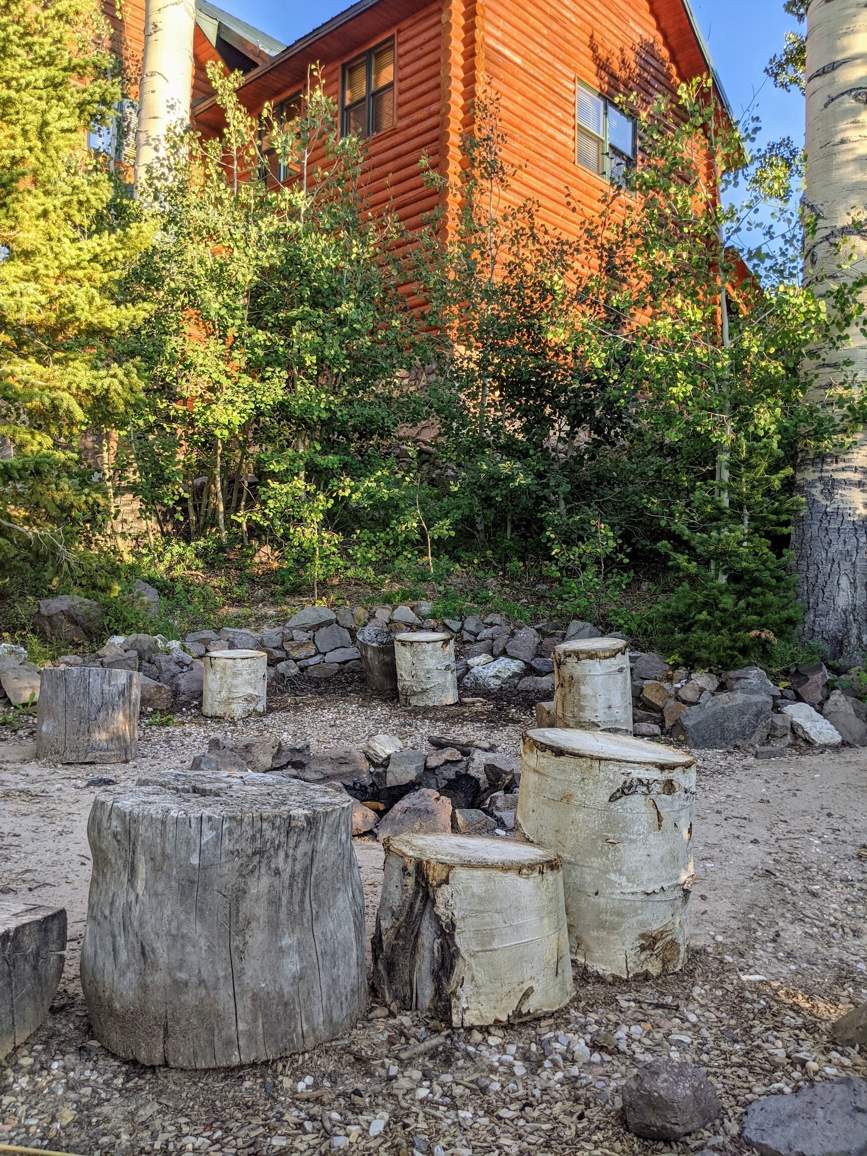A rustic wooden cabin with a stone fire pit surrounded by logs and rocks.