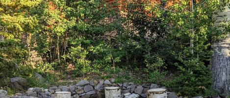 A rustic wooden cabin with a stone fire pit surrounded by logs and rocks.