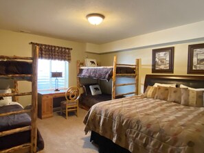 Une chambre avec un lit superposé, un bureau et une chaise, une fenêtre avec des stores et des tableaux encadrés accrochés au mur.