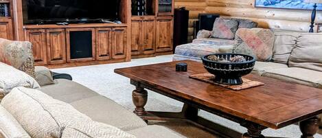 A log cabin interior with a large TV, wooden cabinets, a sofa, and a ceiling fan.