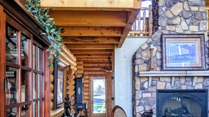 A spacious living area with a wooden floor, a stone fireplace, and a balcony with a wooden railing. - True Ski-in Ski-Out. (Brian Head)