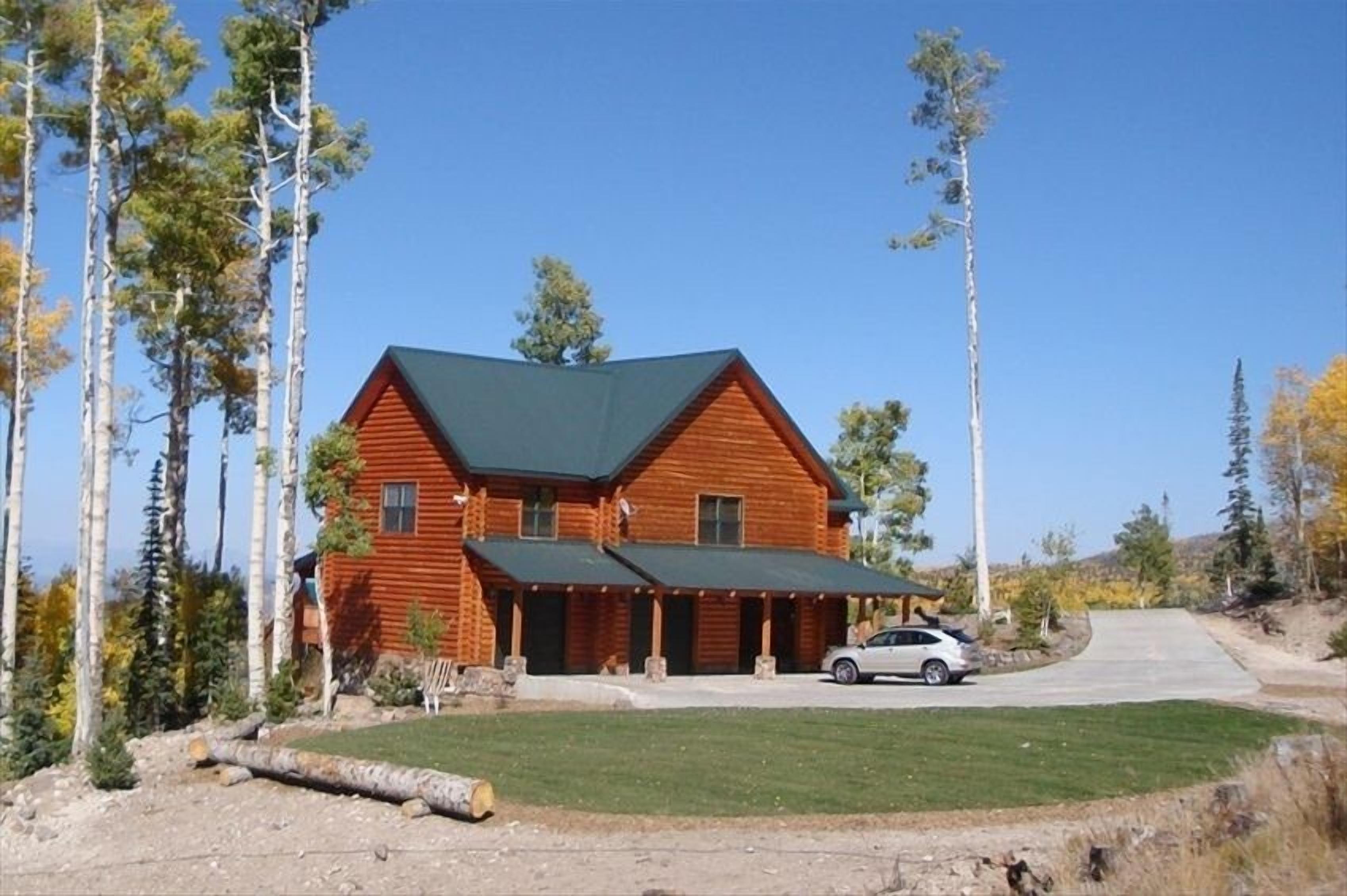 A log cabin with a green roof, a covered porch, and a car parked in front.