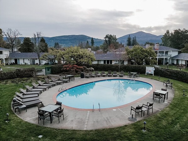 A circular pool surrounded by lounge chairs and tables, with a view of mountains in the background.
