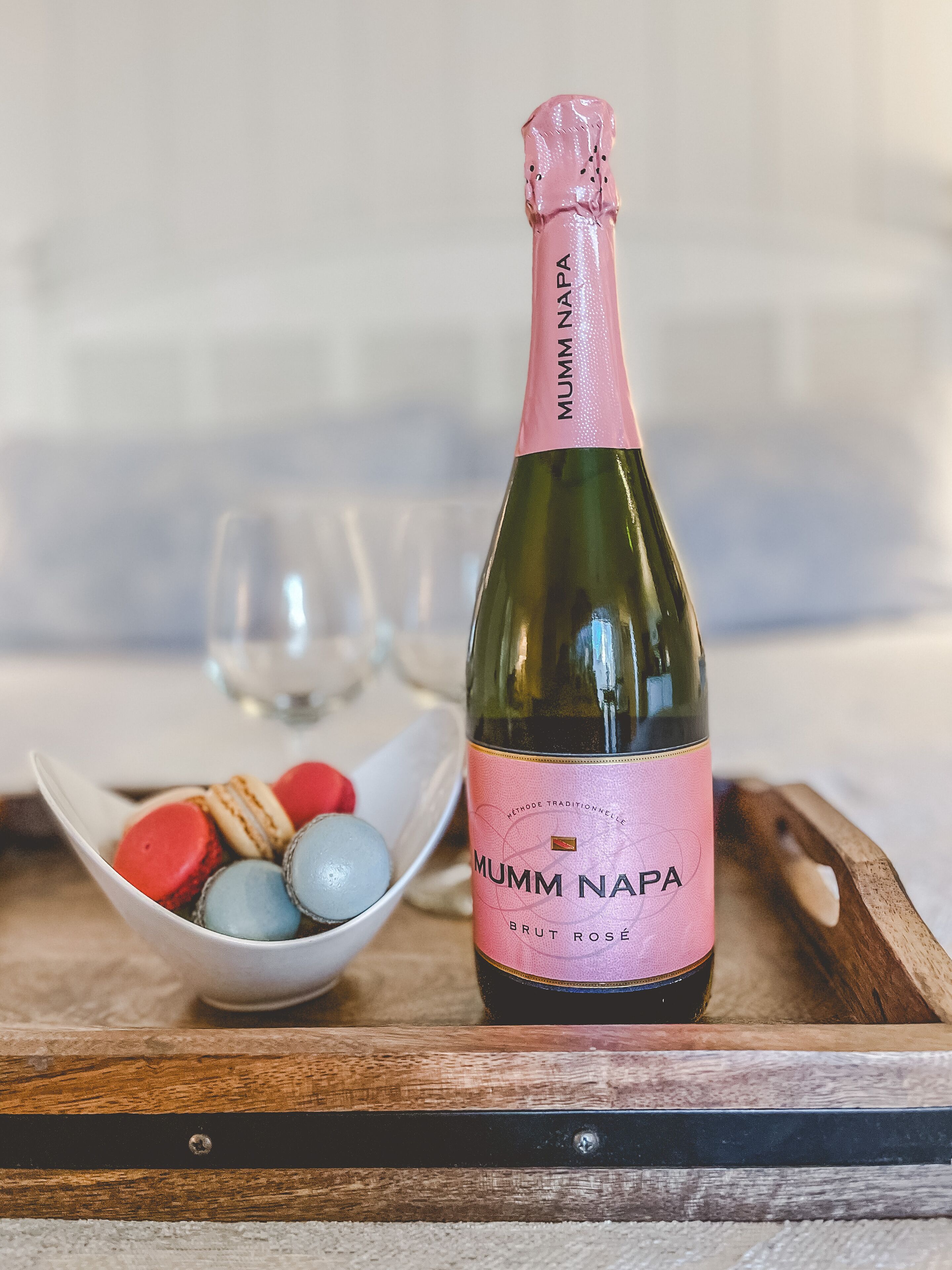 A bottle of Mumm Napa Brut Rosé on a wooden tray with macarons and a glass of wine.