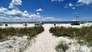 A beach with a sandy path leading to the sea, beach umbrellas, and a lifeguard station. - Ocean Reef Beach-Front, Luxury, Condo with Awesome Balcony, Highly Rated! (Panama City Beach)