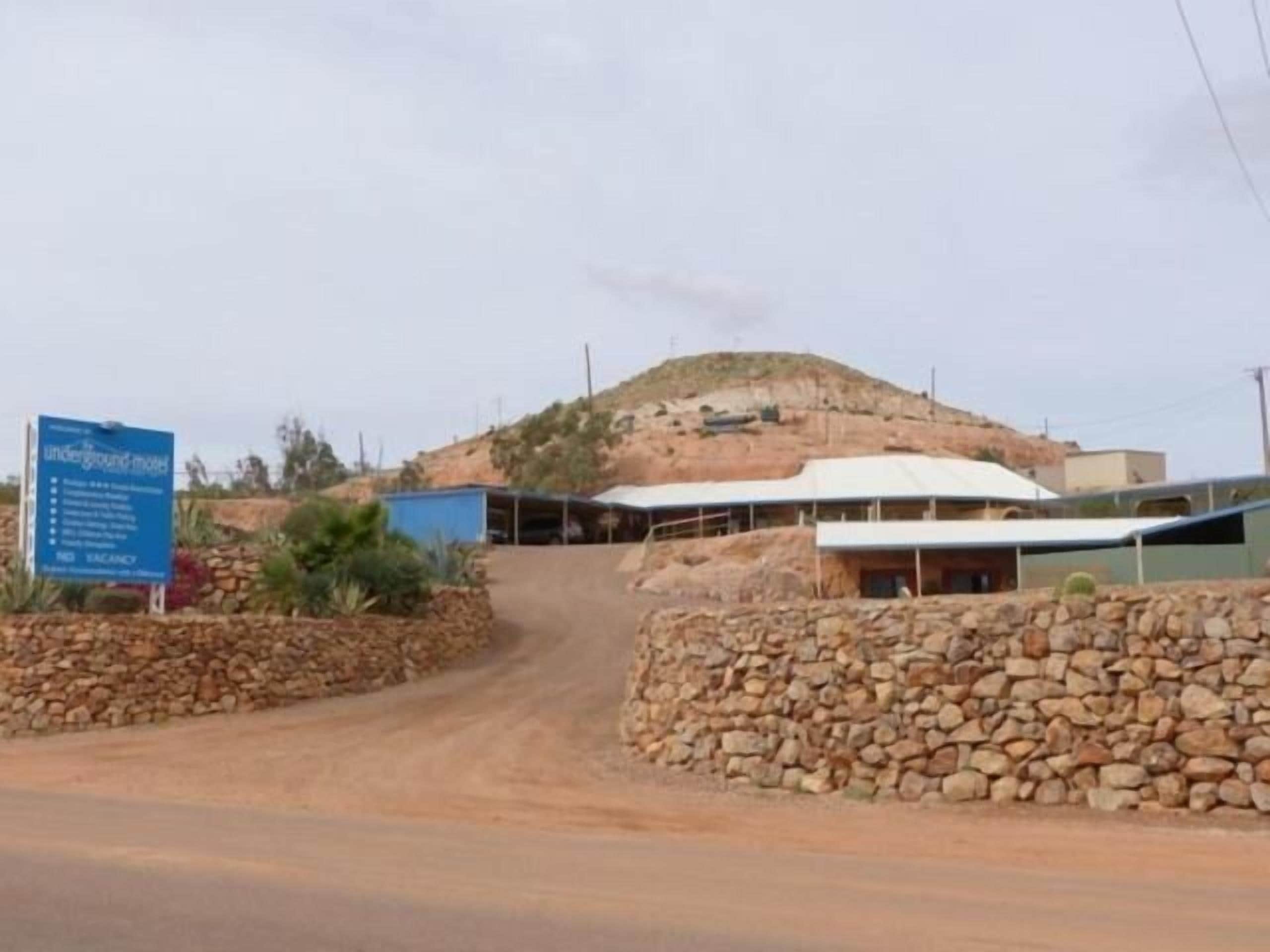 A sign for an underground motel with a dirt road leading to a building with a white roof.