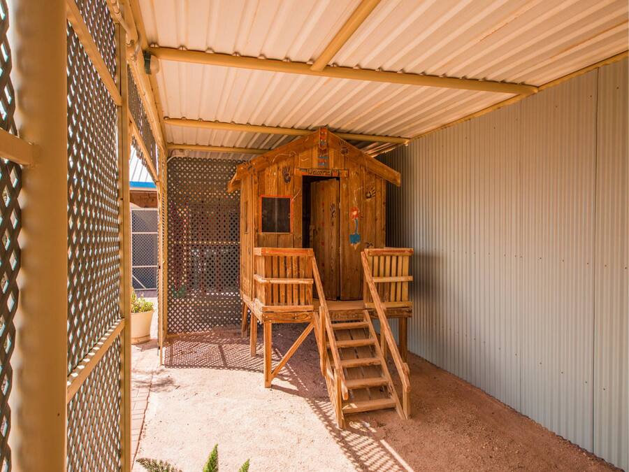 A wooden cabin with a ladder leading to a door, a wooden bench, and a metal fence.