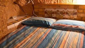 A bed with a colorful striped bedspread in a room with a textured stone wall and a wooden headboard with a cityscape mural.