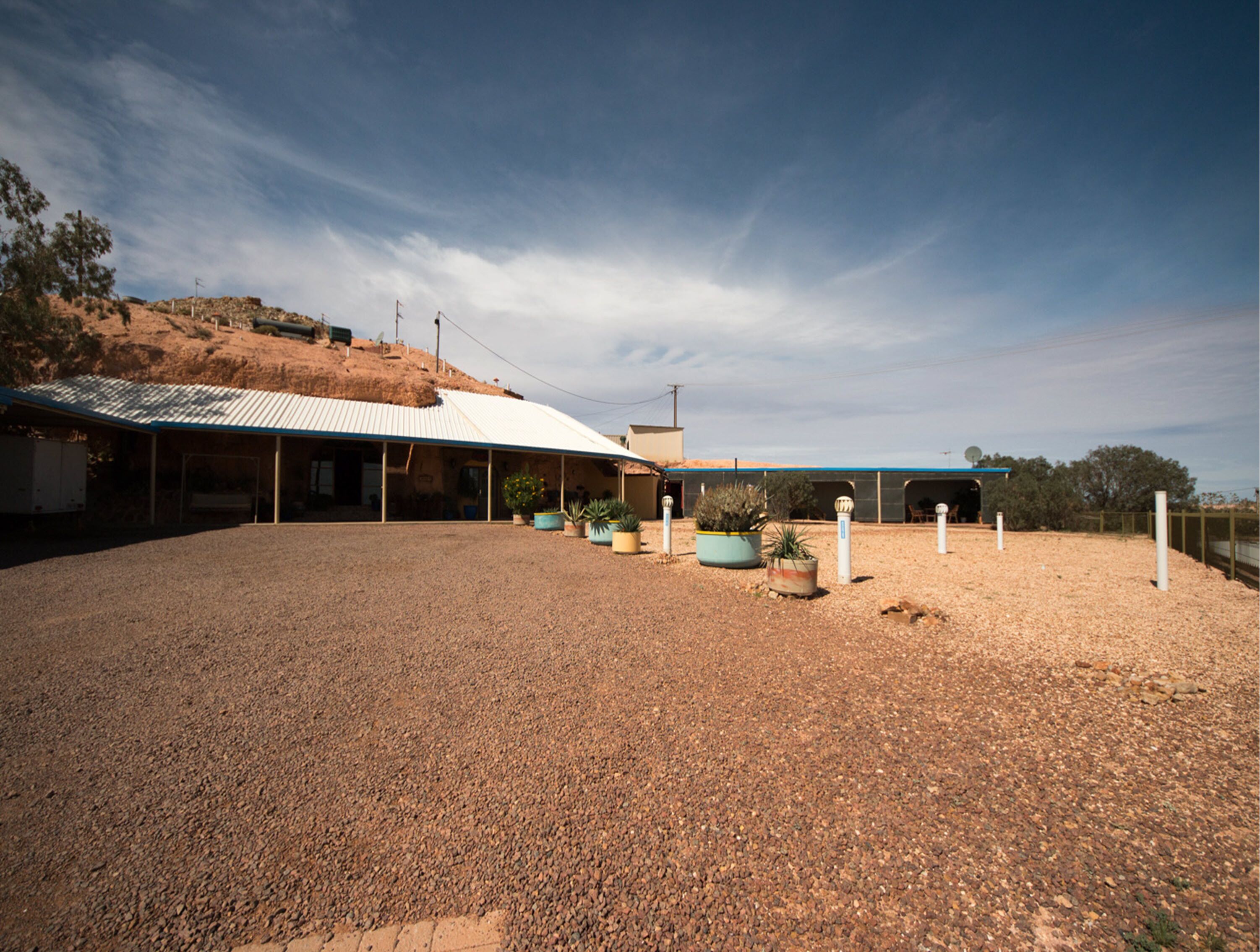 A building with a corrugated metal roof, a gravel driveway, and potted plants.