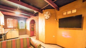 A cozy living room with a striped sofa, a brick fireplace, and a flat-screen TV mounted on the wall. - The Underground Motel (Coober Pedy)
