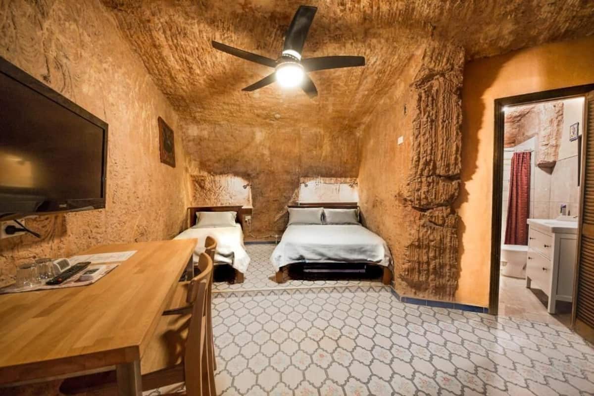 Una habitación con pared de piedra rústica, cama, escritorio y ventilador de techo.
