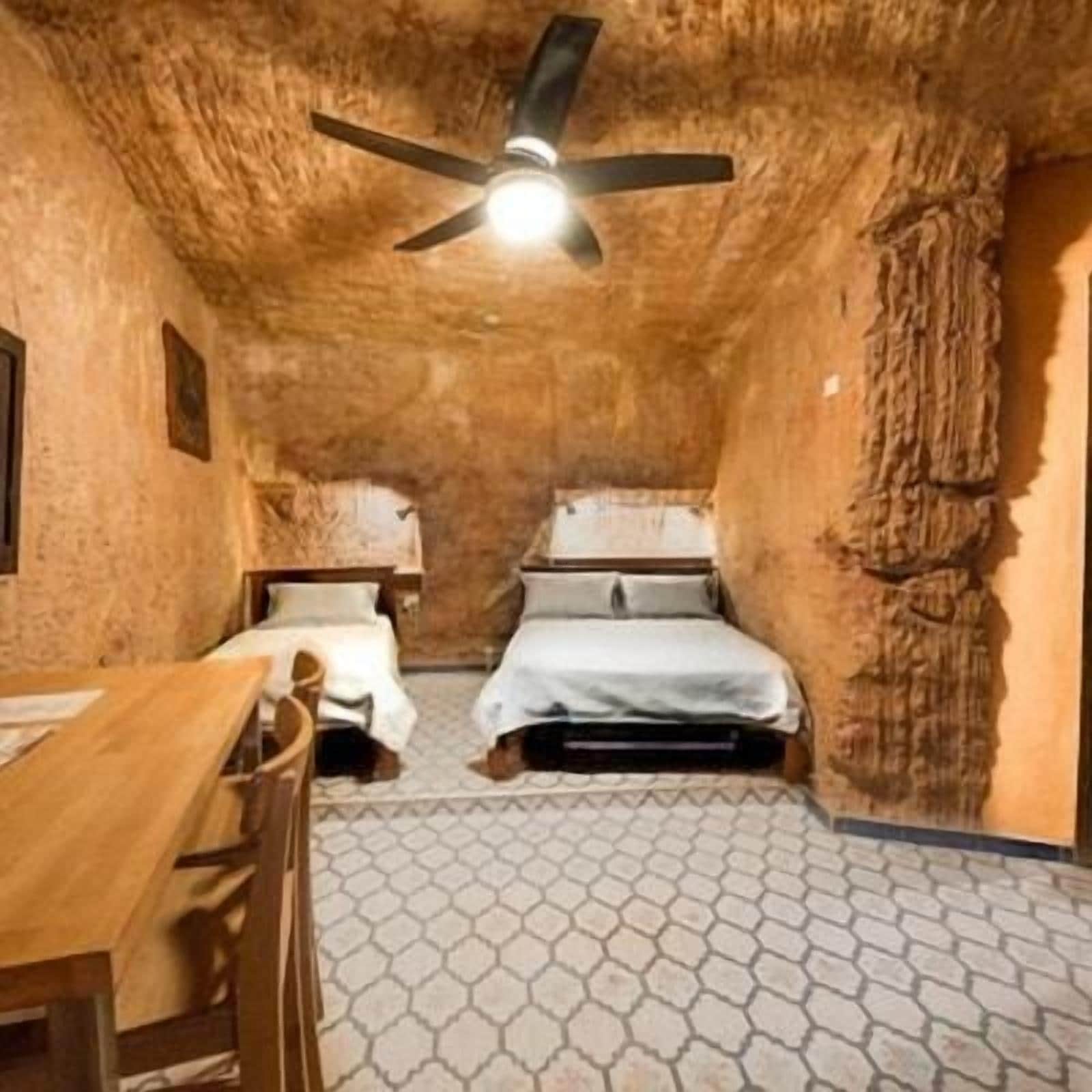 Una habitación con ventilador de techo, dos camas, una mesa y piso con diseño.