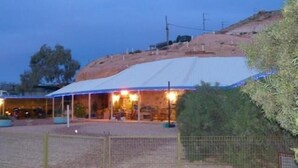 A covered outdoor seating area with tables and chairs, surrounded by a fence. - The Underground Motel (Coober Pedy)