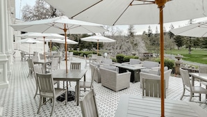 Une terrasse extérieure avec des tables et des chaises blanches, de grands parasols et un sol carrelé.