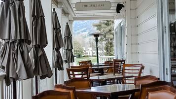 A covered outdoor dining area with tables and chairs, a sign reading "The Grill Bar", and a view of the outdoors.