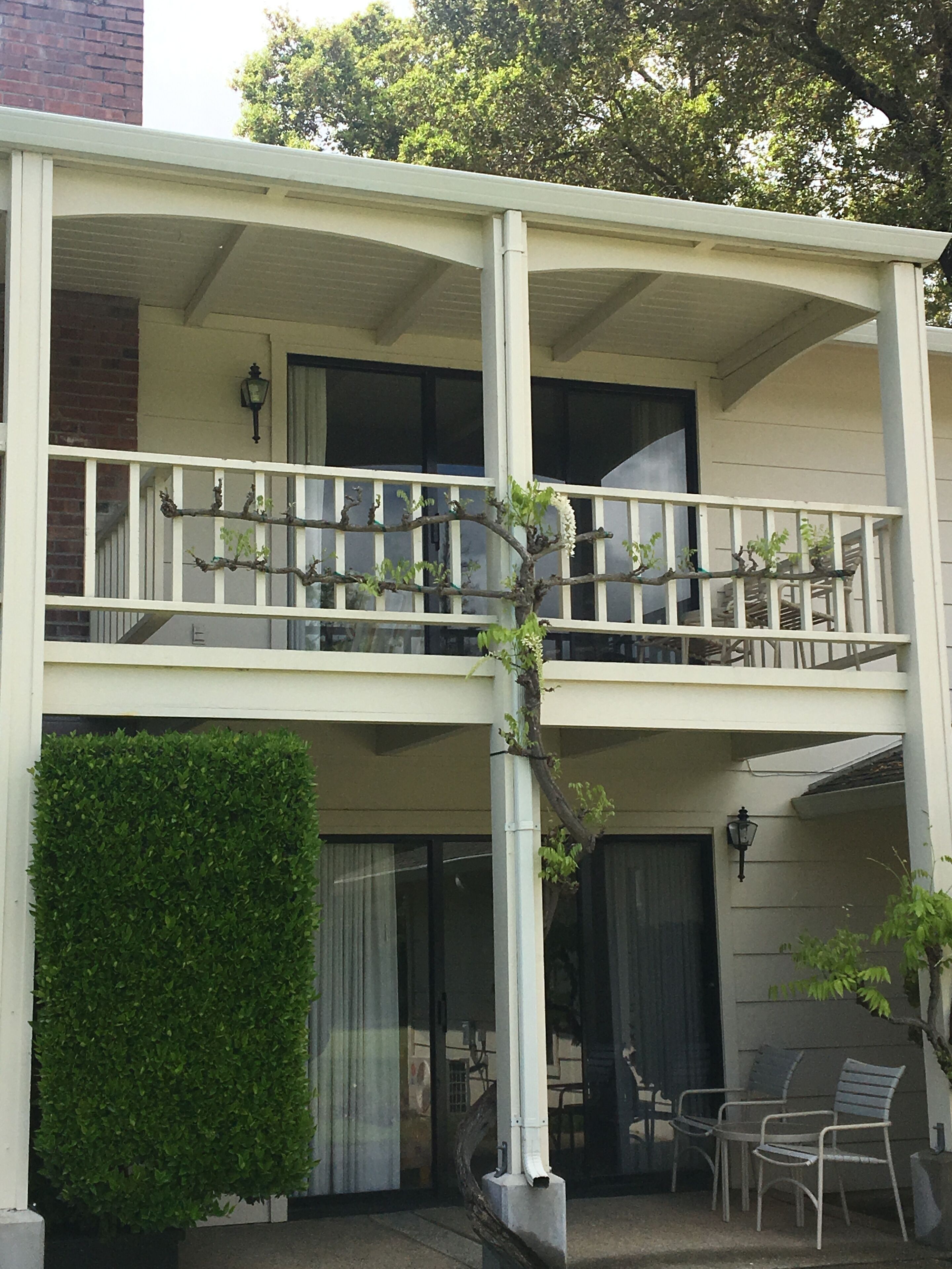 A two-story building with a balcony, a hedge, and outdoor seating.